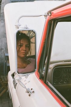 a woman is looking out the window of a red and white truck with her reflection in the mirror