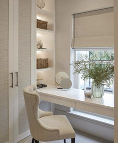 a white desk sitting under a window next to a vase with a plant in it