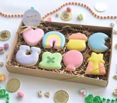 a box filled with lots of decorated cookies on top of a white table next to coins