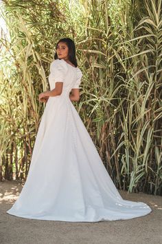 a woman wearing a white dress standing in front of bamboo trees