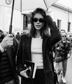 a woman holding an umbrella in the middle of a street with other people walking behind her