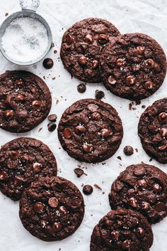 chocolate cookies with sea salt and cocoa chips on white paper next to glass of milk