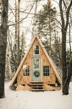 a - frame cabin in the woods with snow on the ground and trees around it