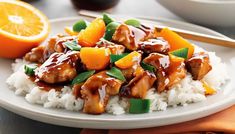 a white plate topped with orange chicken and rice next to chopsticks on a table