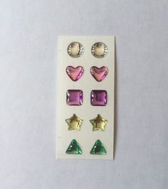 four pairs of studs with different shapes and colors on white paper next to each other