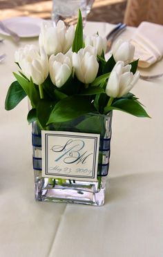 white tulips in a square glass vase on a table at a wedding reception