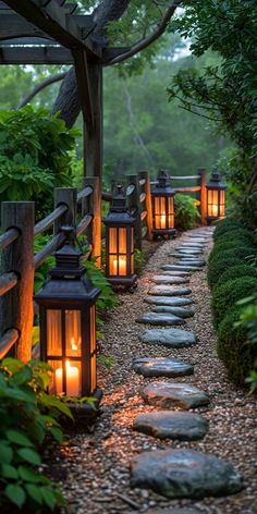 lanterns lit up in the middle of a path between trees and rocks, along with stepping stones