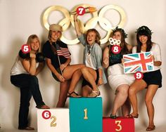 four women standing on top of a podium holding up their numbers and olympic signs in front of them