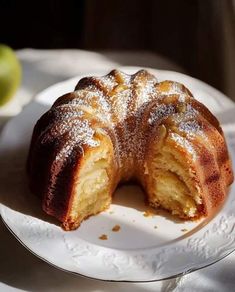 a bundt cake on a plate with powdered sugar and an apple in the background