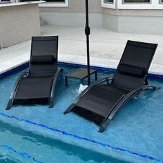 two lounge chairs sitting under an umbrella next to a swimming pool with blue water in it