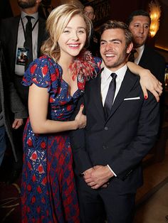 a man in a suit and tie standing next to a woman wearing a floral dress