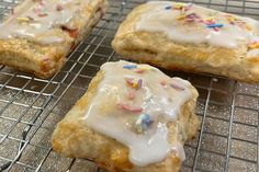 three pastries with icing and sprinkles on a cooling rack