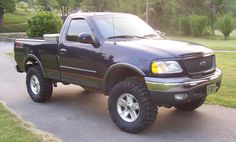 a black truck parked on the side of a road next to a lush green field