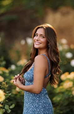 a beautiful young woman in a blue dress posing for the camera with flowers behind her