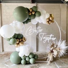 a balloon arch with white, green and gold balloons