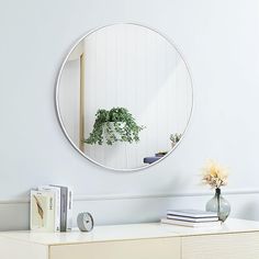 a round mirror on the wall above a dresser with books and flowers in vases