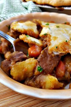 a bowl filled with meat and potatoes on top of a wooden table next to a fork