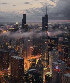 the city is lit up at night with fog in the air and skyscrapers on both sides