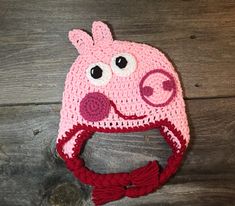 a crocheted hat with a pig face on the front and side, sitting on top of a wooden surface