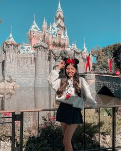 a woman standing in front of a castle with minnie mouse ears on her head wearing a sweater