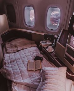 an airplane bed with two pillows and a book on it next to the window in the cabin