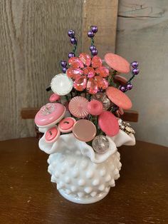 a white vase filled with lots of pink and purple flowers on top of a wooden table