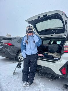 a woman standing next to a car in the snow with skis on her head