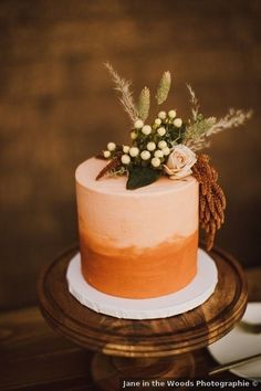 a close up of a cake on a wooden table with white flowers and greenery