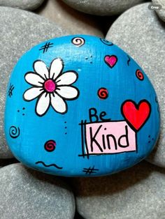 a painted rock with the words be kind and a flower on it surrounded by rocks