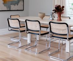 a dining room table with four chairs and a vase on the table in front of it