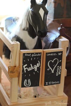 a black and white horse standing next to a wooden sign with chalk writing on it