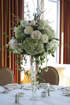 a vase filled with white flowers sitting on top of a table next to plates and silverware