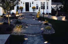 a white house is lit up with lights and landscaping lighting in front of the house