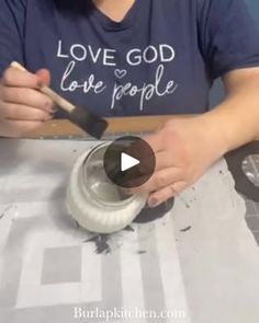 a woman is painting the inside of a jar with white paint and a black brush