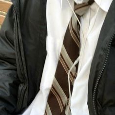 a man wearing a jacket and tie sitting on a bench with his hands in his pockets