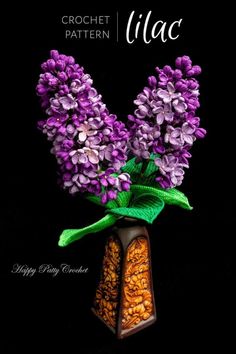 a vase filled with purple flowers sitting on top of a black table next to a green leaf