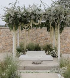 an outdoor ceremony setup with white flowers and greenery on the walls, in front of a stone wall