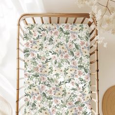 a baby's crib with flowers and leaves on the cover, next to a wicker basket