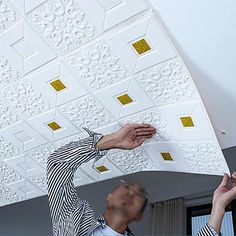 two people reaching up to paint a ceiling with gold and white designs on the ceiling