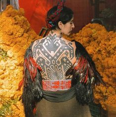 a woman with tattoos on her back standing in front of yellow and orange flower arrangements