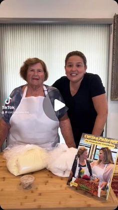 two women are standing behind a table with food on it and dvd's in front of them