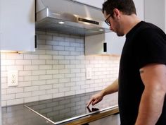 a man standing in front of a stove top oven holding a piece of metal on it's side