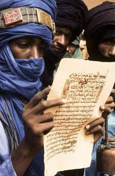 two men in turbans are holding up a piece of paper with writing on it