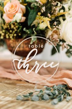 the table name plate is surrounded by flowers and greenery on top of a wooden table