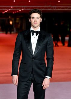 a man in a tuxedo standing on a red carpet with his hands in his pockets