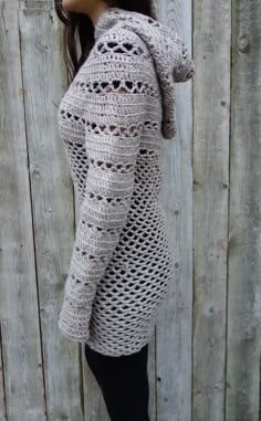 a woman wearing a crocheted sweater and leggings standing in front of a fence