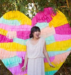 a woman standing in front of a giant heart made out of colorful paper strips and fringes