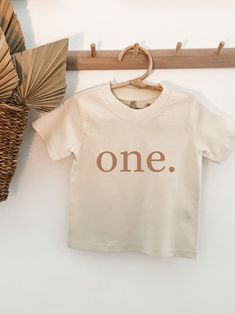 a t - shirt with the word one hanging on a clothes rack next to a fan