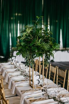 a long table with white linens, gold chairs and greenery in vases