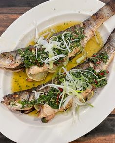 two fish on a white plate with sauce and garnishes, sitting on a wooden table